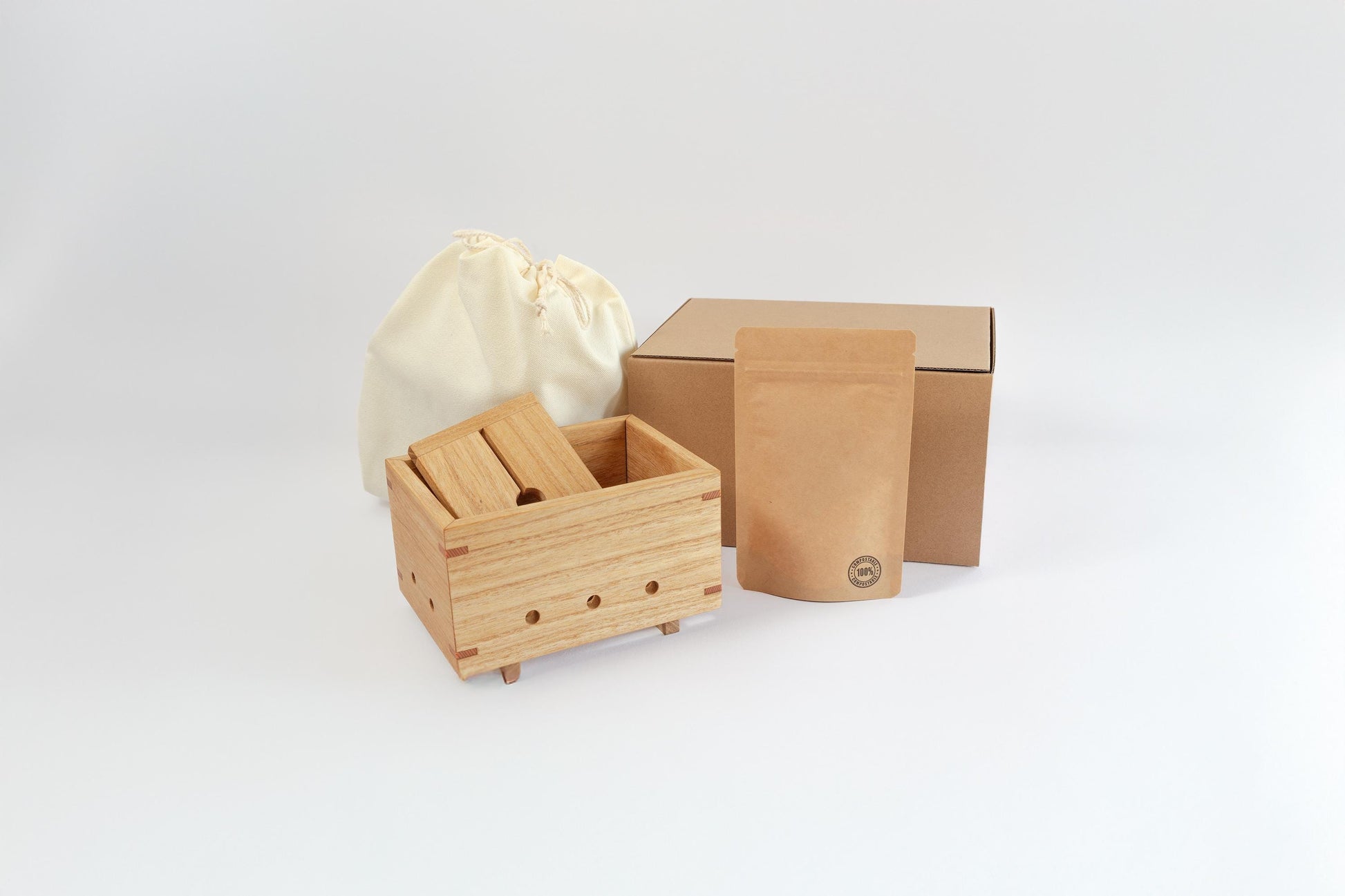 Wooden tofu press, calico bag, Kraft food pouch and wooden box on a white background. Depicts plastic free packaging for Tofu Press Australia.