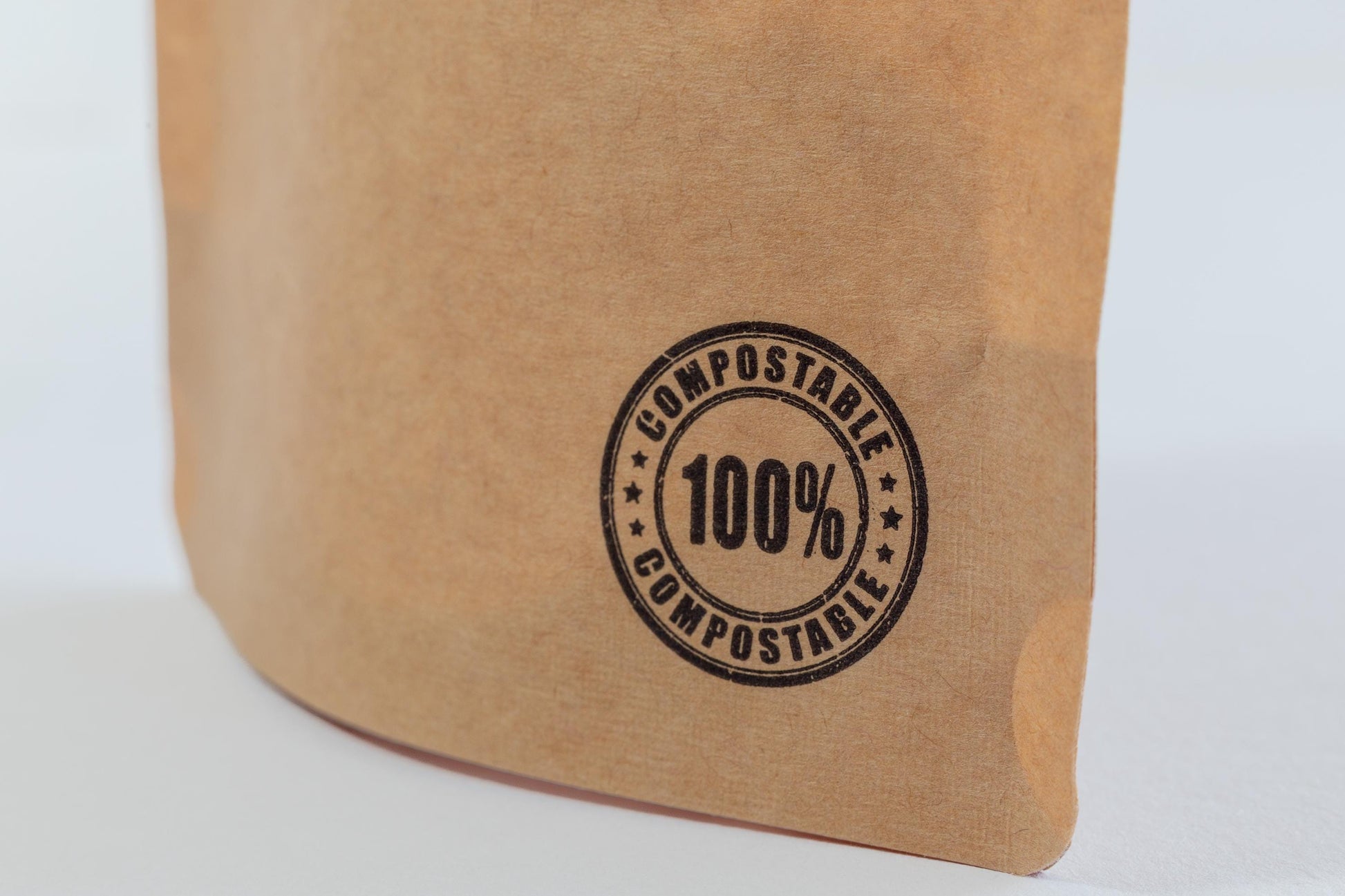 Close up of '100% compostable' stamp on the bottom of a Kraft paper food pouch containing gypsum powder.