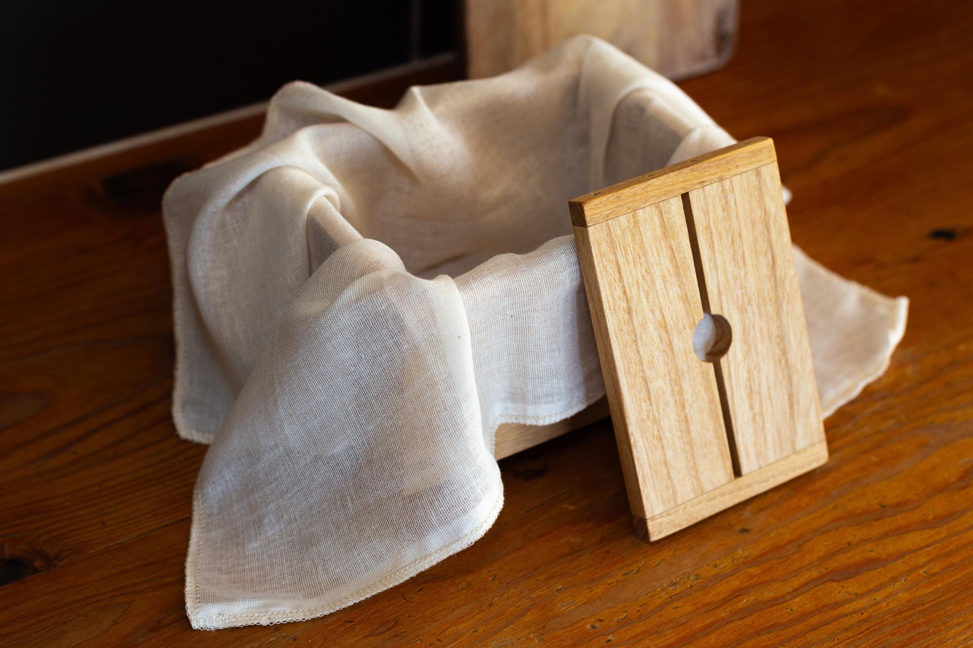 Close up of a muslin cloth-lined wooden tofu press and lid by Tofu Press Australia on a rustic kitchen bench.