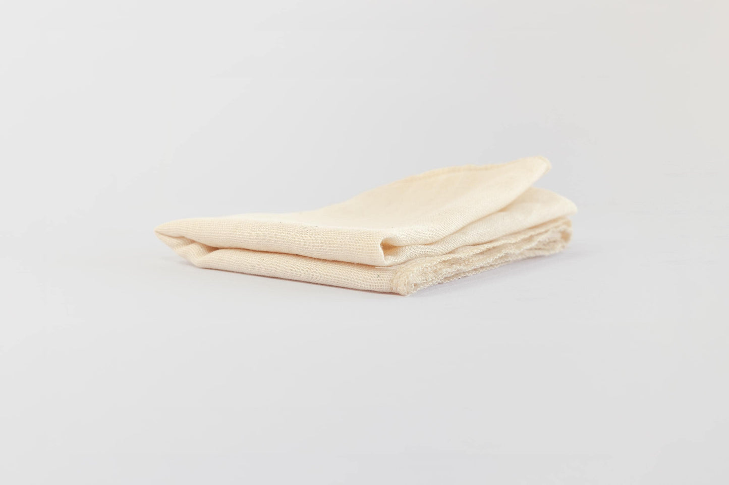 Close up of folded, hemmed natural, food-safe muslin cloth for soy milk straining and tofu making on a white background.