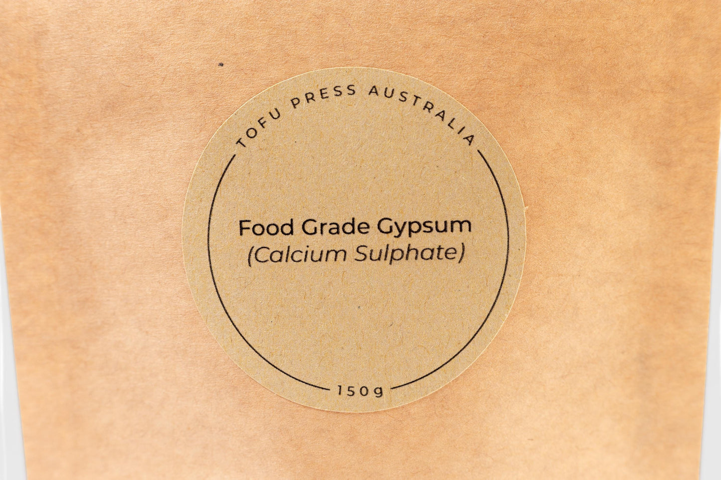 Close up of round brown-paper label on a biodegradable Kraft paper food pouch reading 'Tofu Press Australia. Food Grade Gypsum (Calcium Sulphate). 150g'.