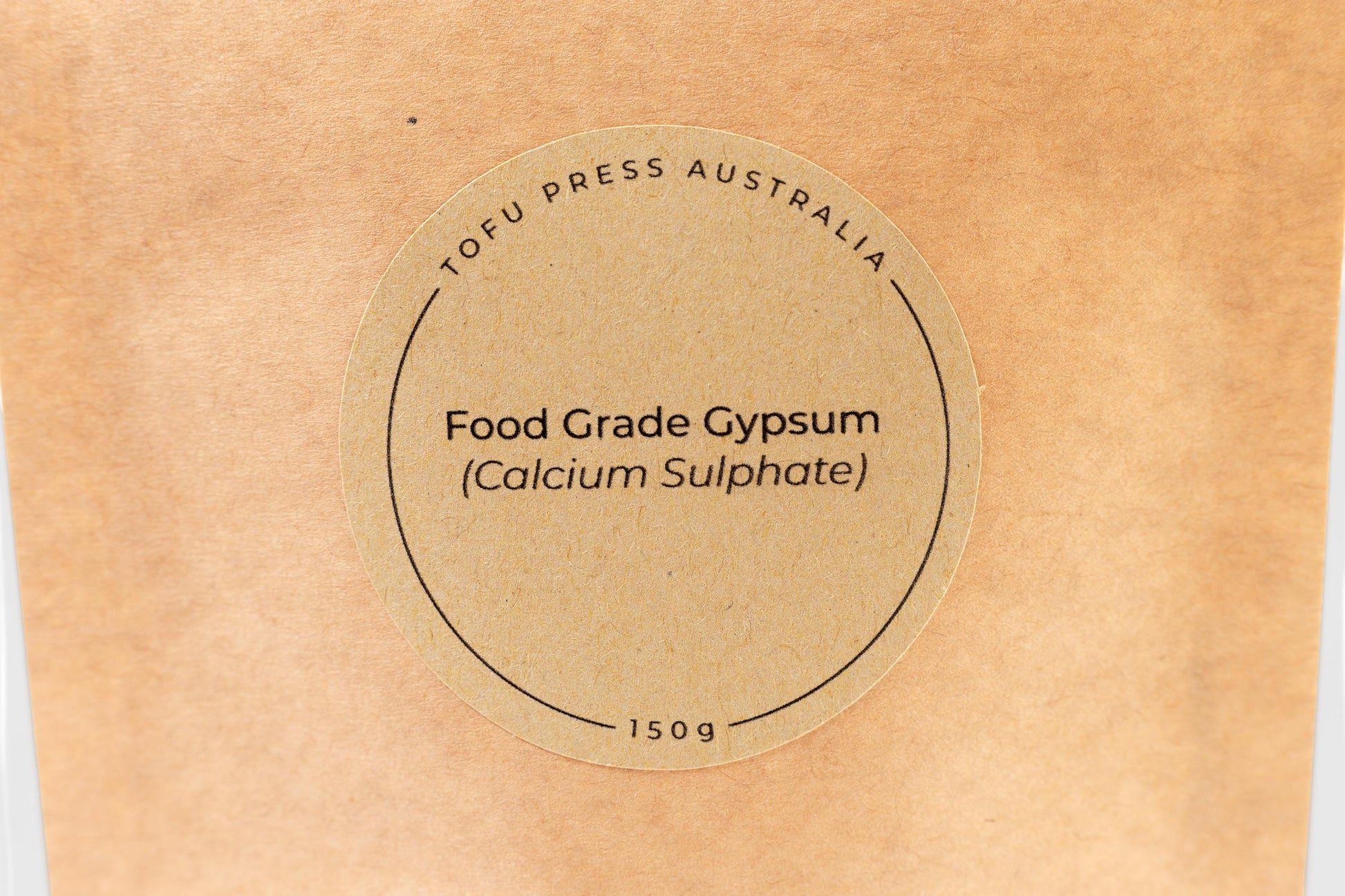 Close up of round brown-paper label on a biodegradable Kraft paper food pouch reading 'Tofu Press Australia. Food Grade Gypsum (Calcium Sulphate). 150g'.