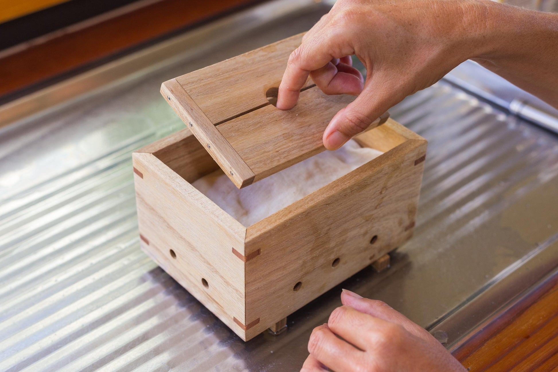 Close up of person removing lid from a wooden tofu press, revealing the tofu inside.